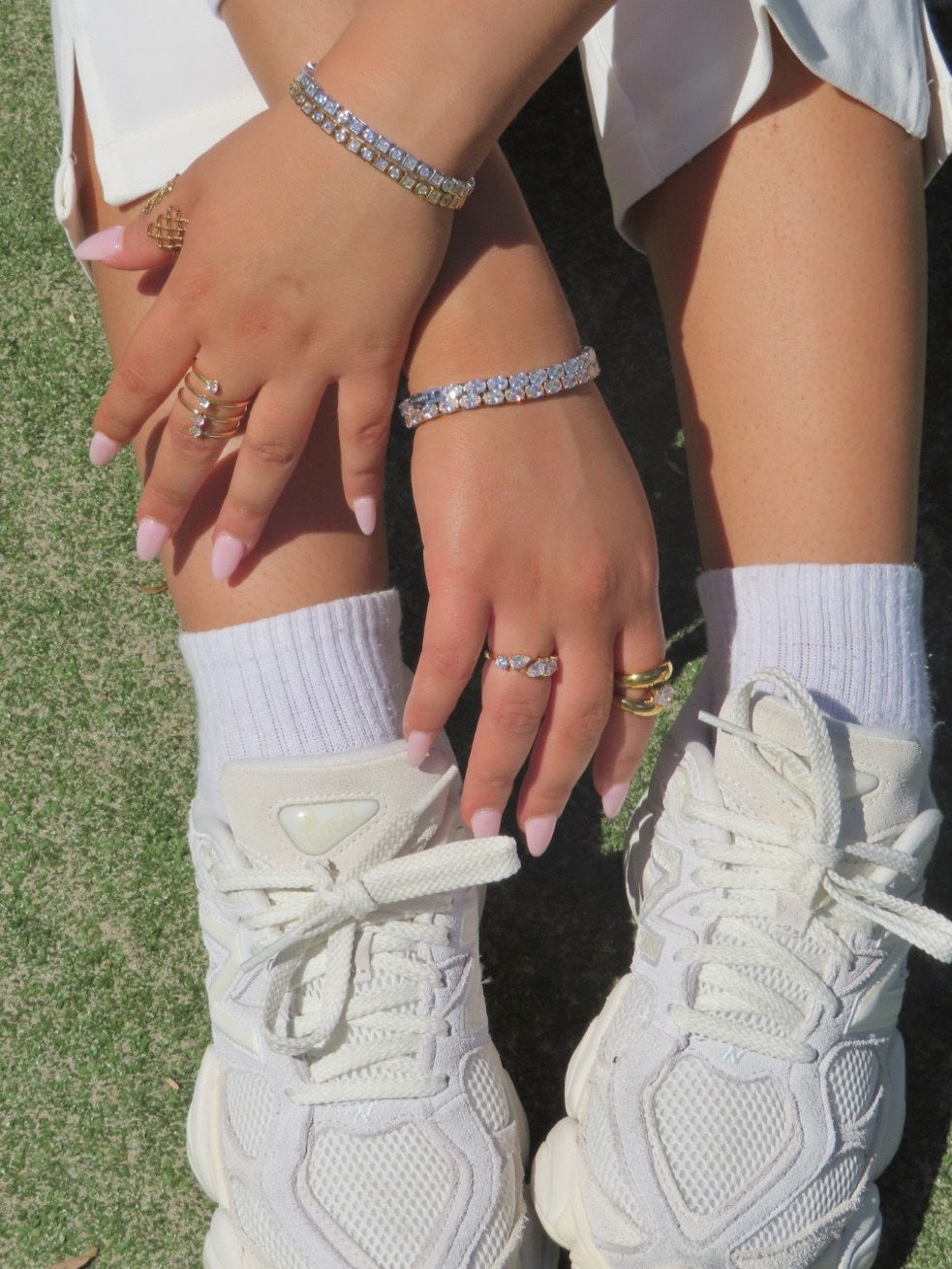 Gold tennis bracelets and rings stacked on both wrists