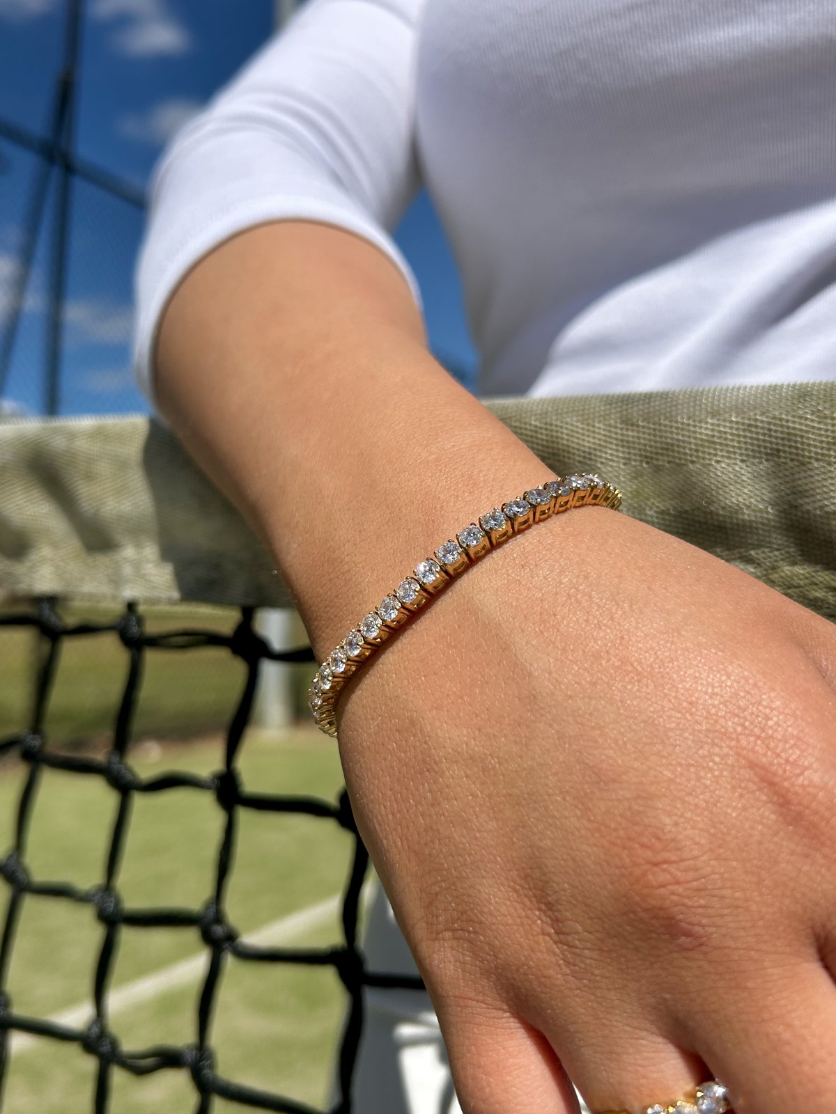 Gold tennis bracelet on a wrist resting on a tennis net